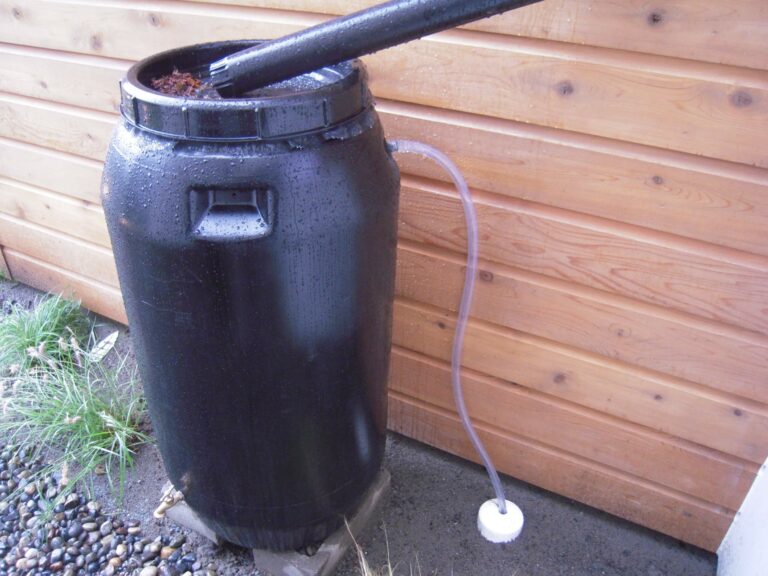 A rain barrel on the exterior of a house. Useful to collect water and prevent water damage on the outside of a home