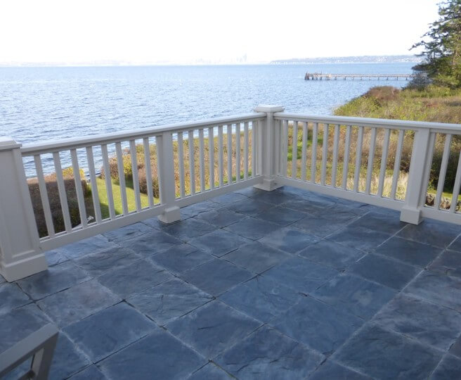 Stone tiling with a white wooden fence surrounding the deck. Water in the background