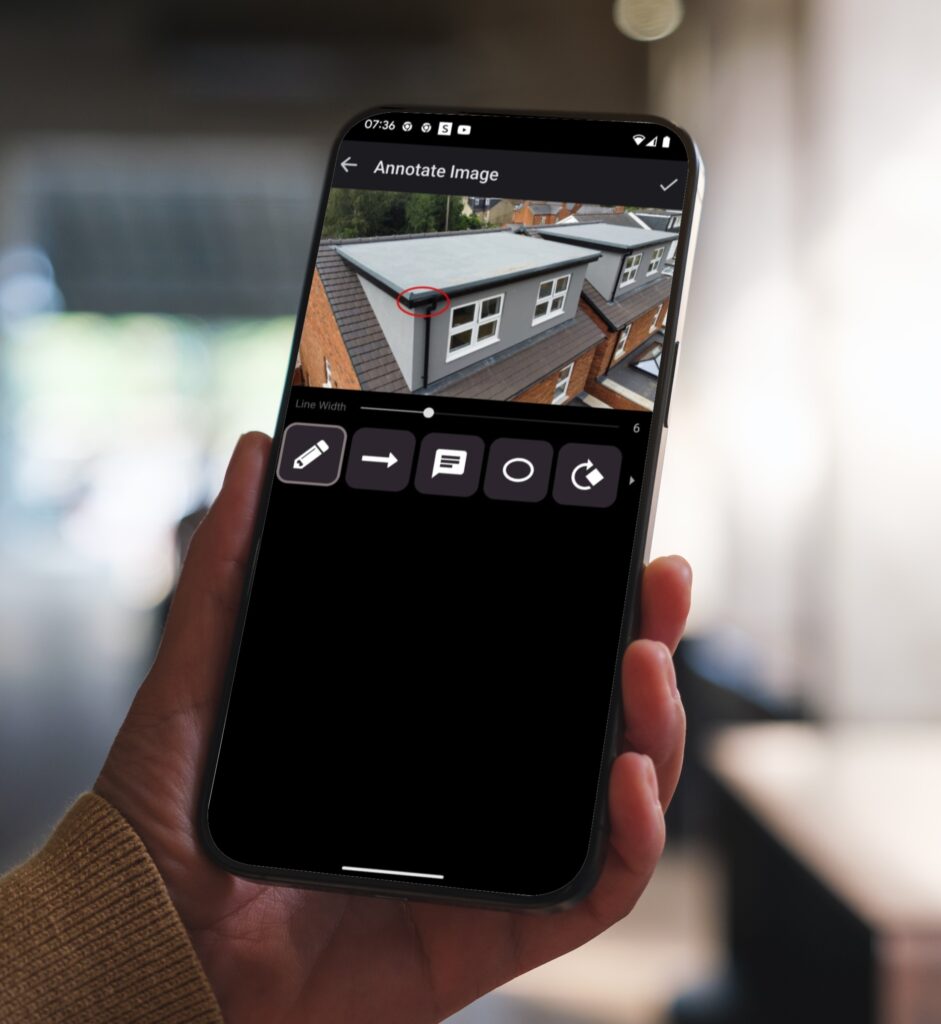 A hand holds a mobile phone that is displaying a ScribeWare UK Surveyor Report showing an issue with a roof
